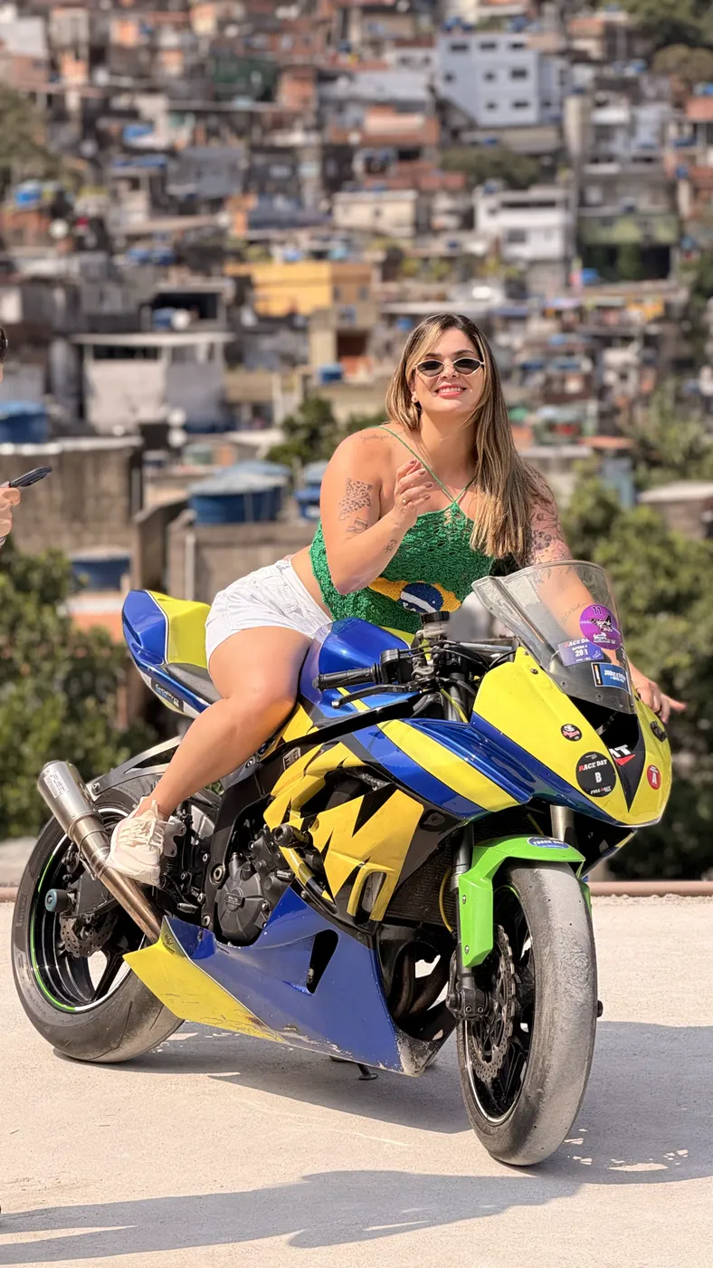 Turista sentada na moto esportiva no alto da Rocinha, com a comunidade ao fundo.