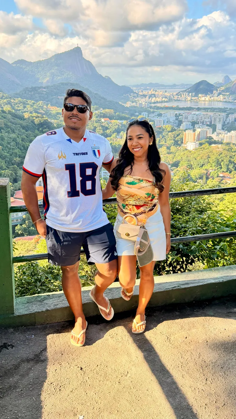 Casal de turistas no mirante, com a mata e as montanhas do Rio ao fundo.