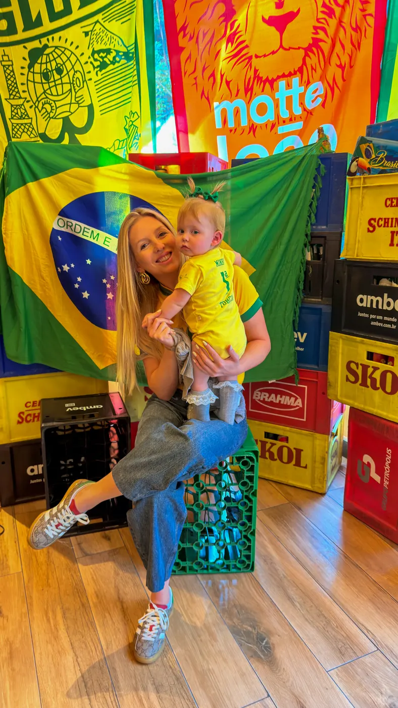 Mãe e criança em frente a um painel com a bandeira do Brasil, num comércio local da Rocinha.