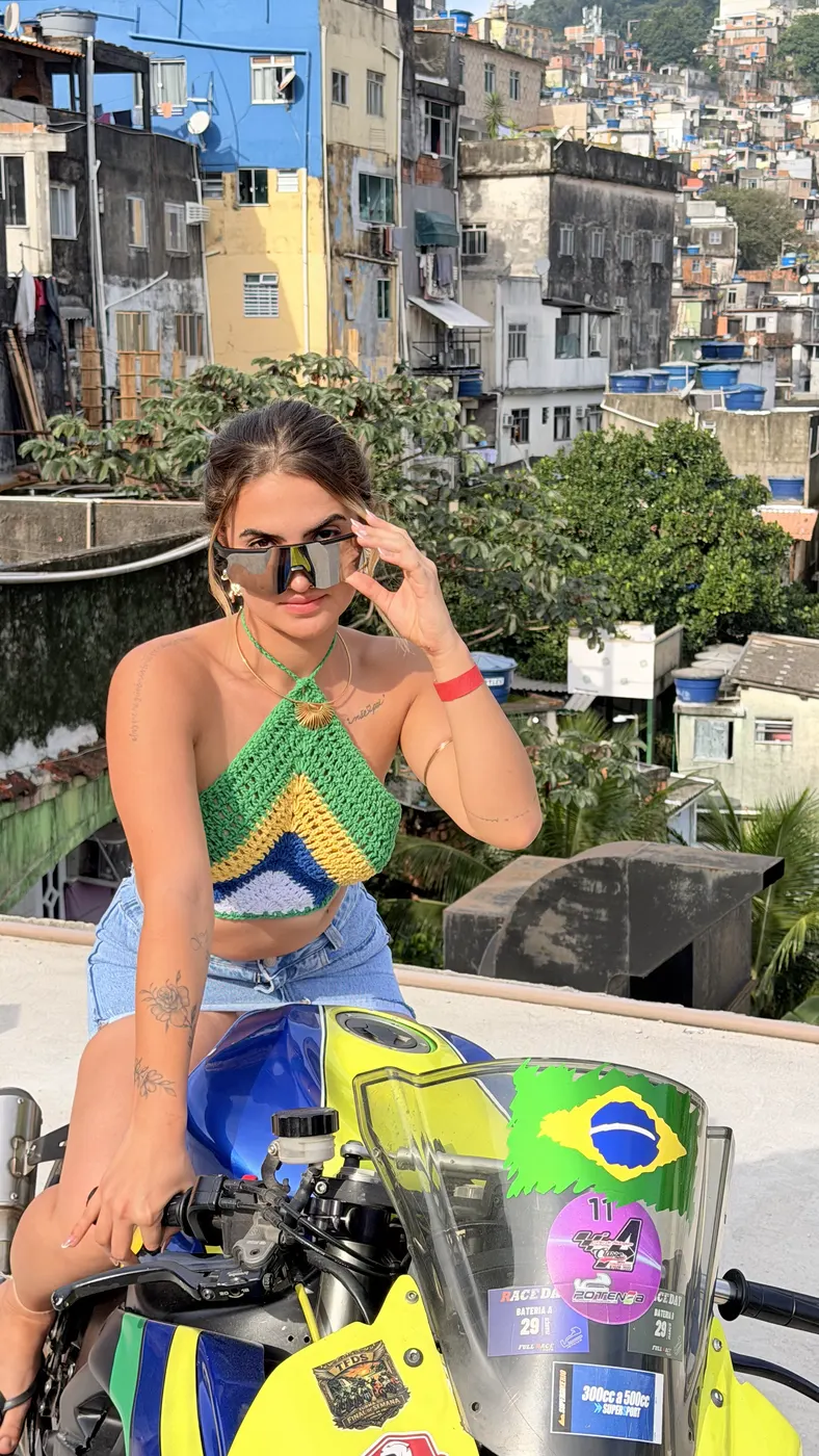 Turista apoiada na moto decorada, com as casas coloridas da Rocinha atrás.