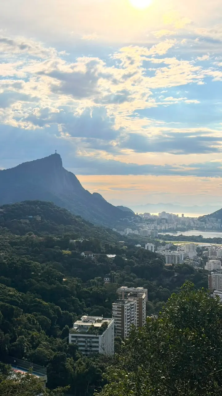 Pôr do sol visto do alto da Rocinha, com a mata, os prédios e as montanhas em silhueta.